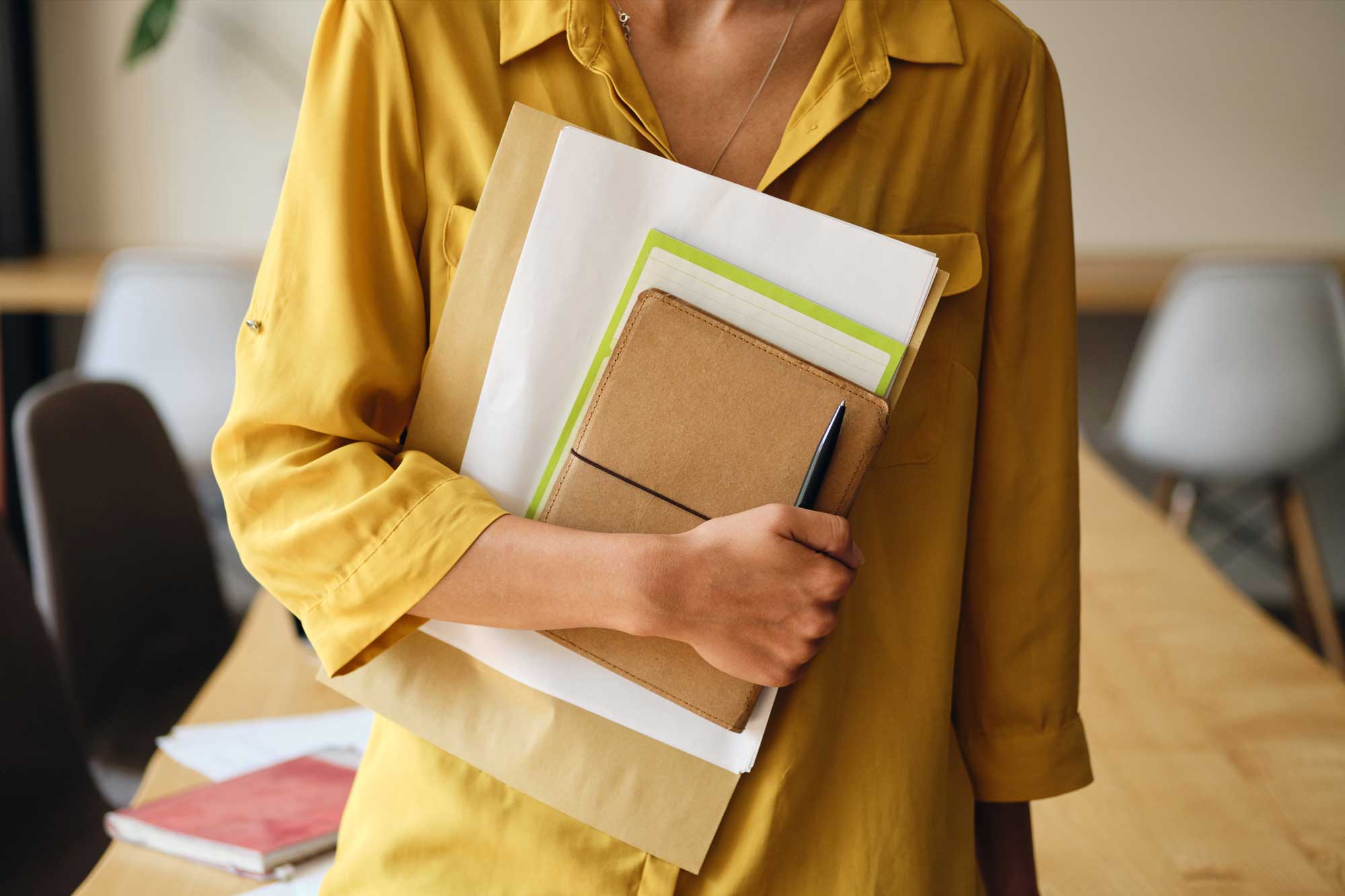 Close up woman in yellow shirt holding notepad and papers in hand in modern office